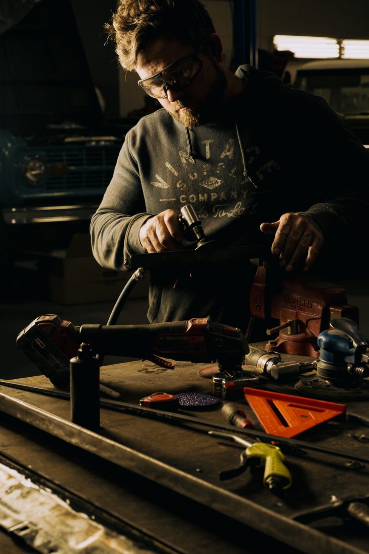 Fabricator grinding metal at a workbench in a restoration shop