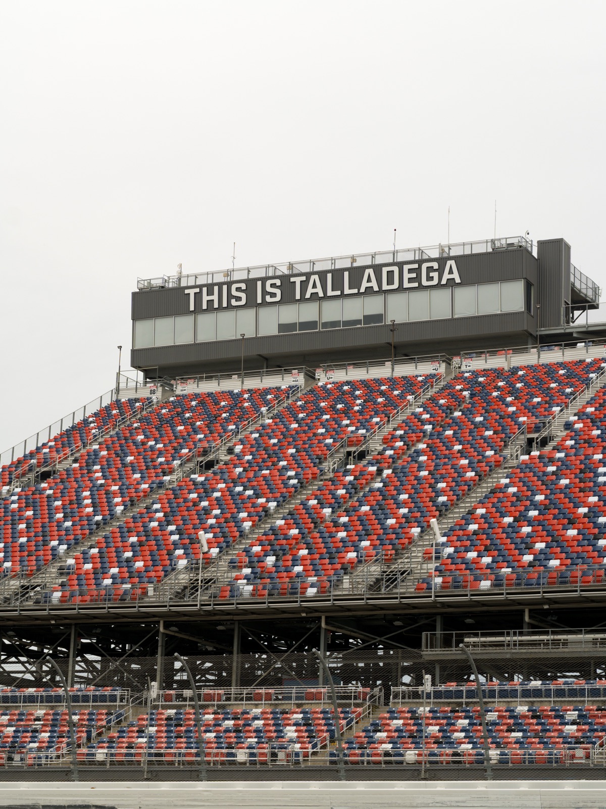 Empty red, white, and blue grandstands at Talladega Superspeedway beneath the 'This is Talladega' tower