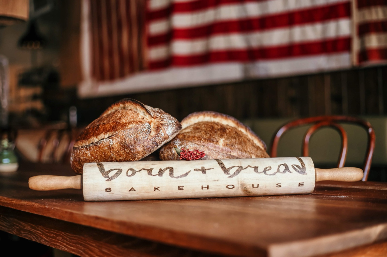 Two sourdough loaves and a branded rolling pin on a wood table at Born + Bread Bakehouse