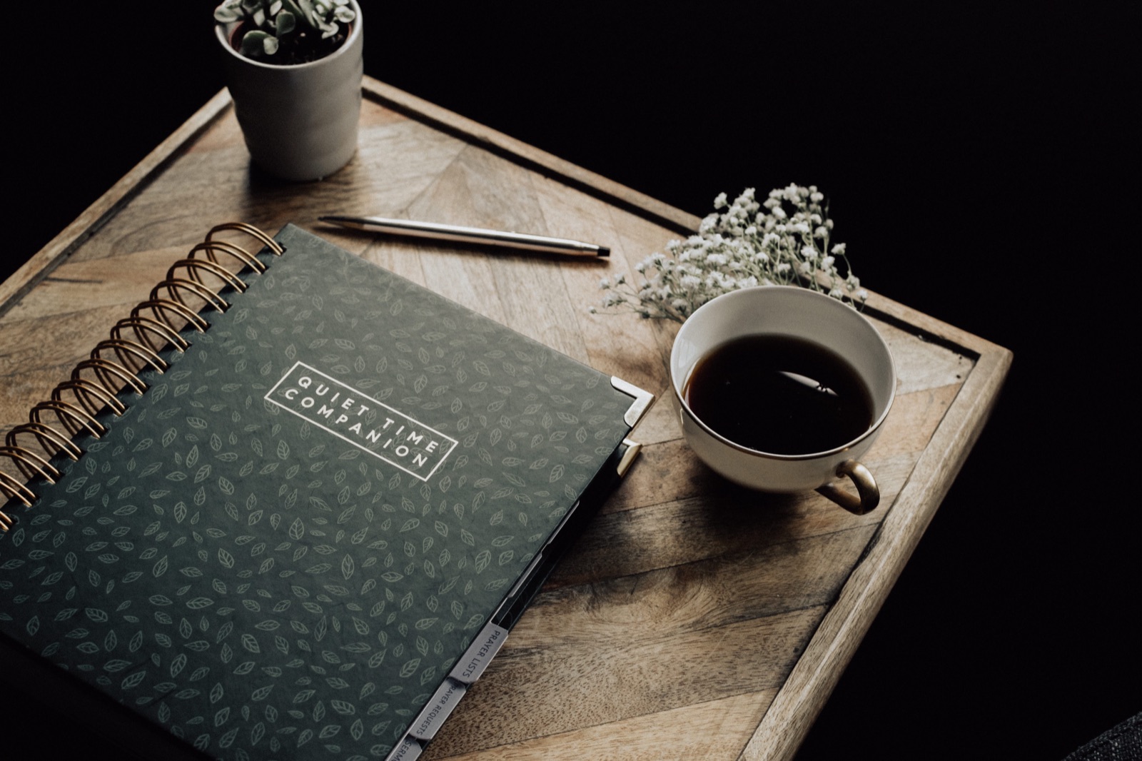 Quiet Time Companion journal, a cup of coffee, and a small plant styled on a wood surface