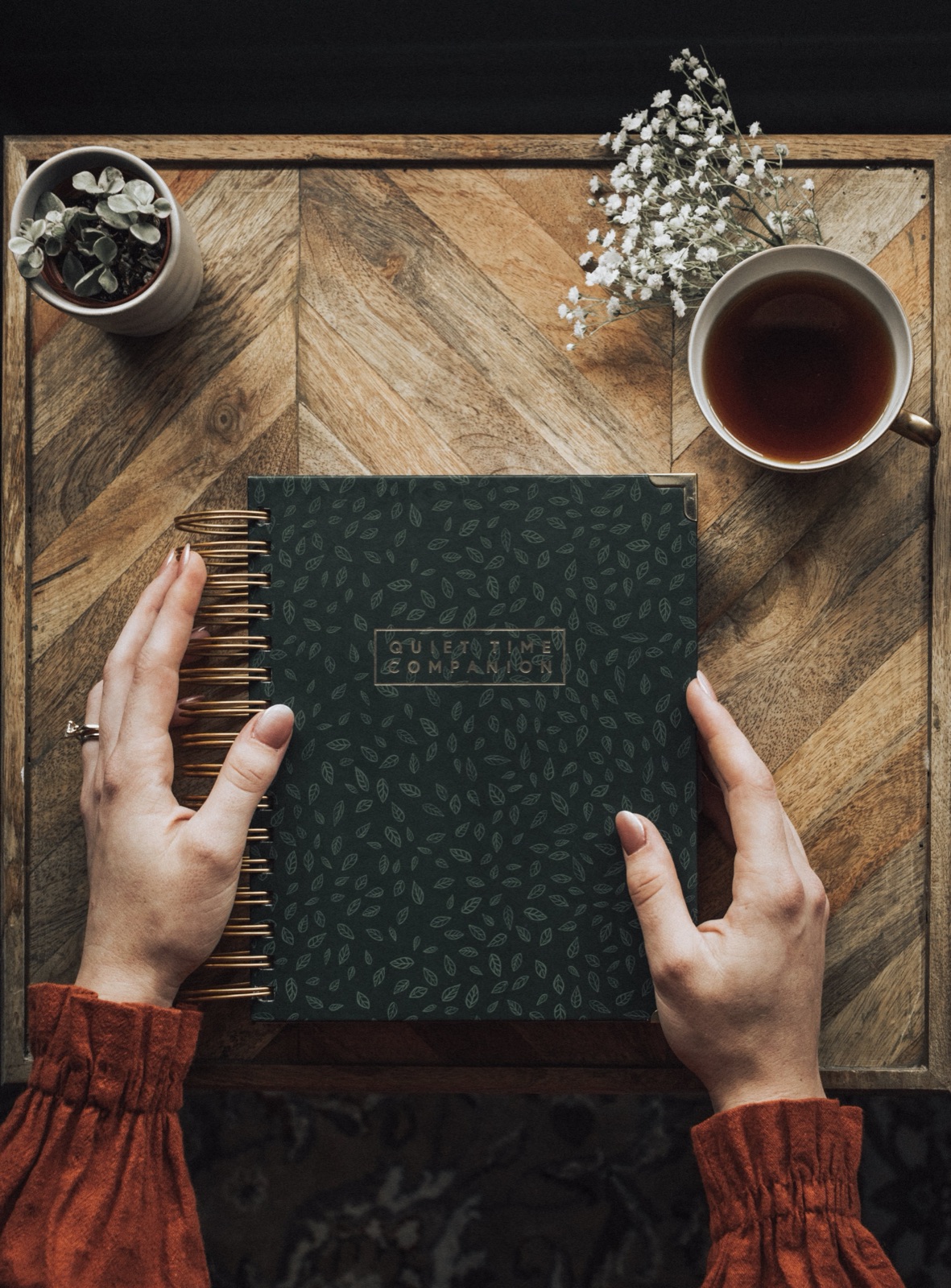 Hands holding the Quiet Time Companion journal on a chevron wood tray beside tea